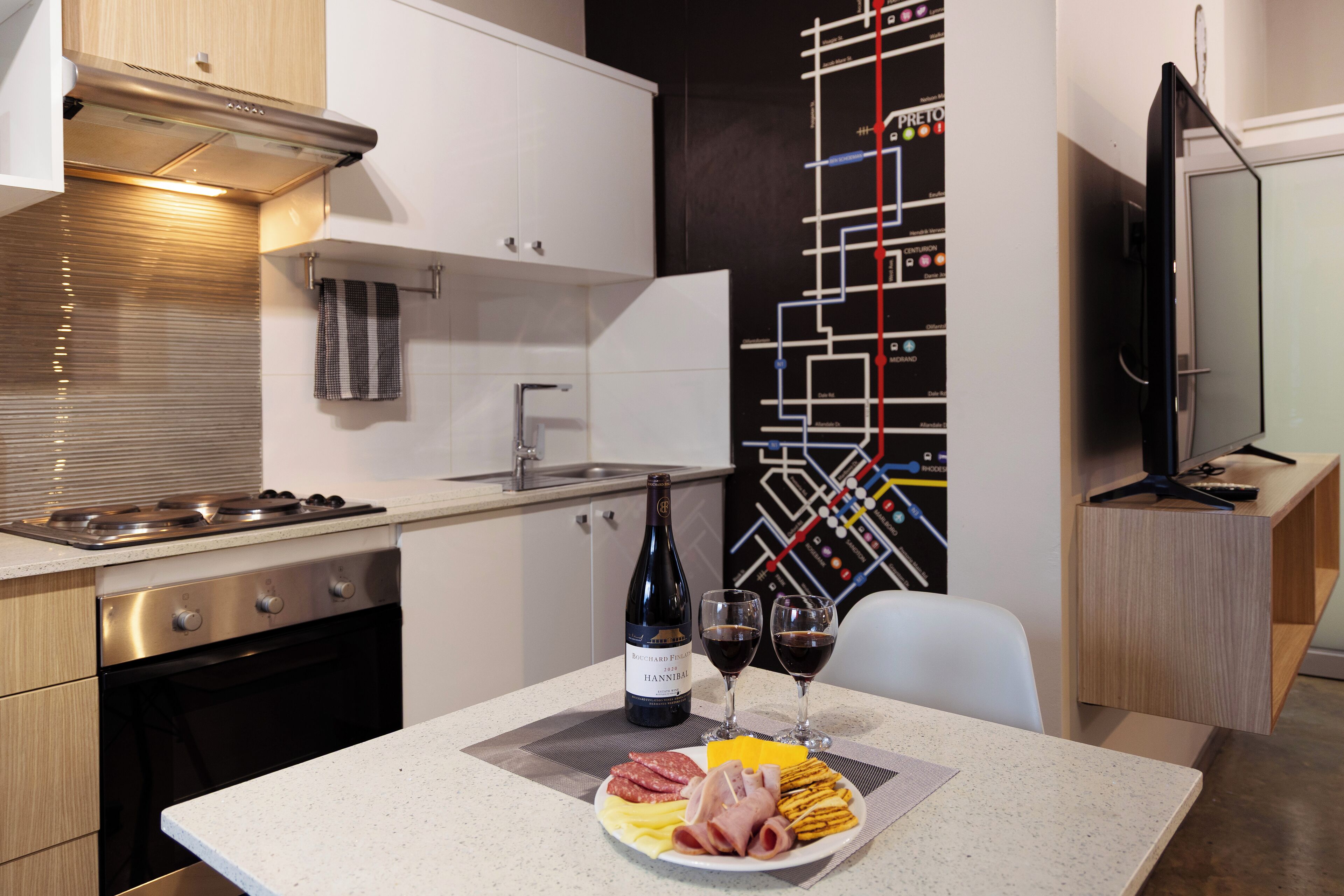 A modern kitchen with a dining area, featuring a stainless steel stove, a wine bottle, and glasses on the table.