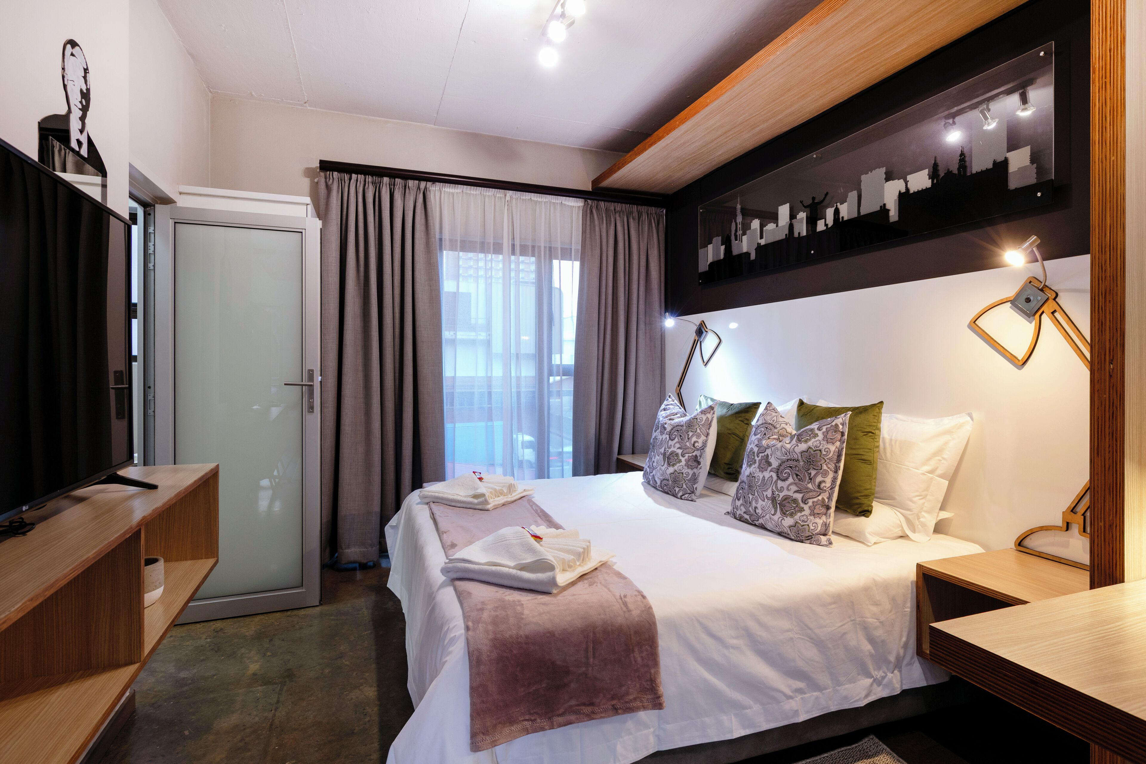A modern hotel room with a bed, bedside table, and a television on a stand.