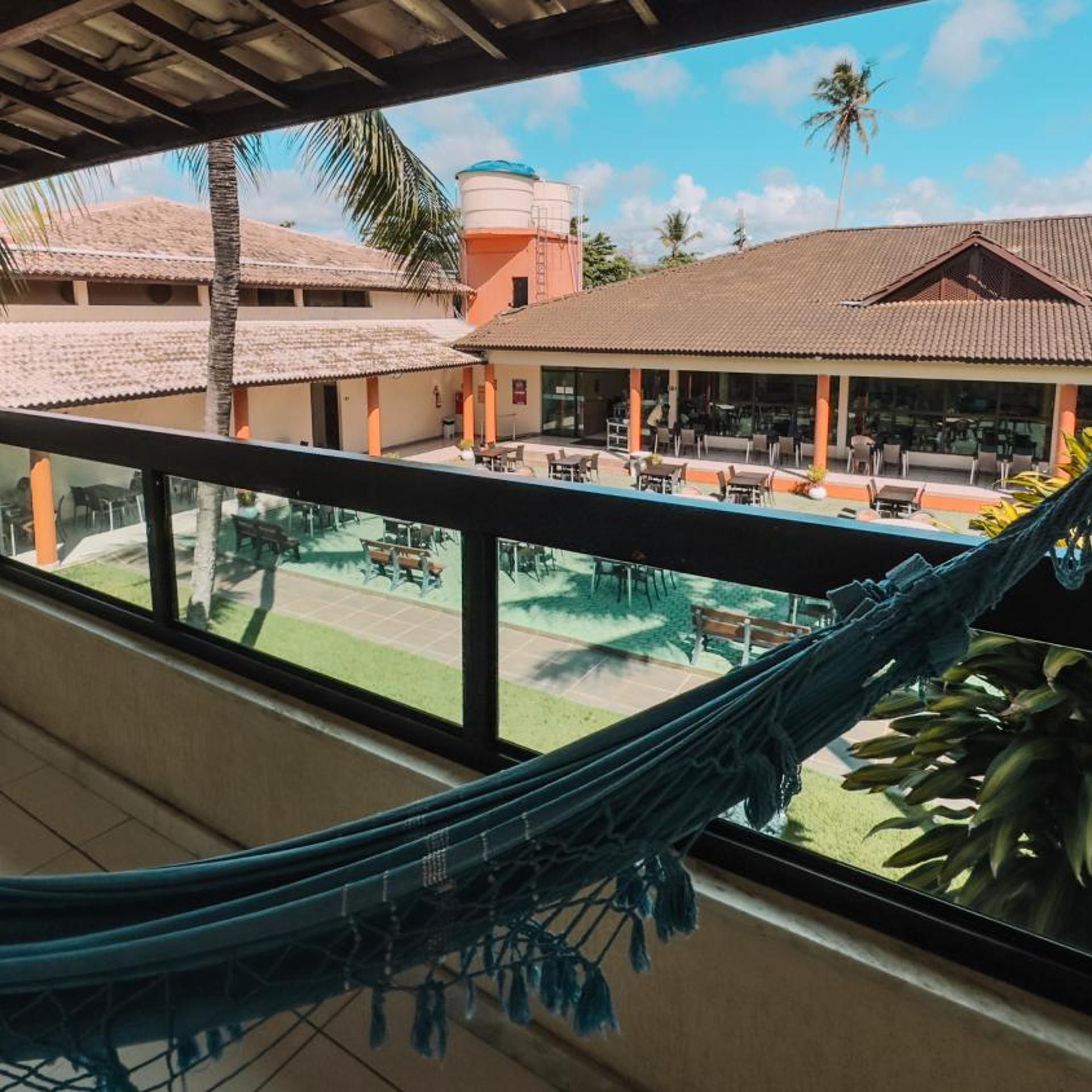 Varanda com rede, com vista para área de piscina, mobiliário externo e edifício com telhado cerâmico.