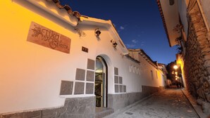 Una estrecha calle adoquinada con un edificio identificado como "Tika Hostel", que presenta fachada de piedra, entrada en arco y tejado de azulejos.