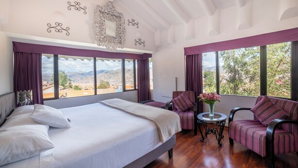 Un dormitorio amplio con una cama grande, dos sillones, una mesita y vistas al exterior.