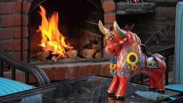 A rustic outdoor seating area with a brick fireplace, a decorative bull sculpture, and a glass table.