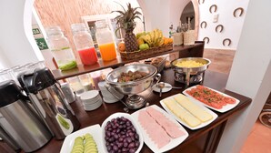Un bufé con diversas opciones de comida, como aguacate en rodajas, aceitunas, jamón y queso.