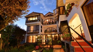 Una casa de dos pisos con un balcón, un jardín y una escalera.
