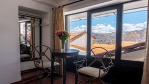 Una habitación con un ventanal grande, una mesa redonda con un florero y dos sillas de metal.
