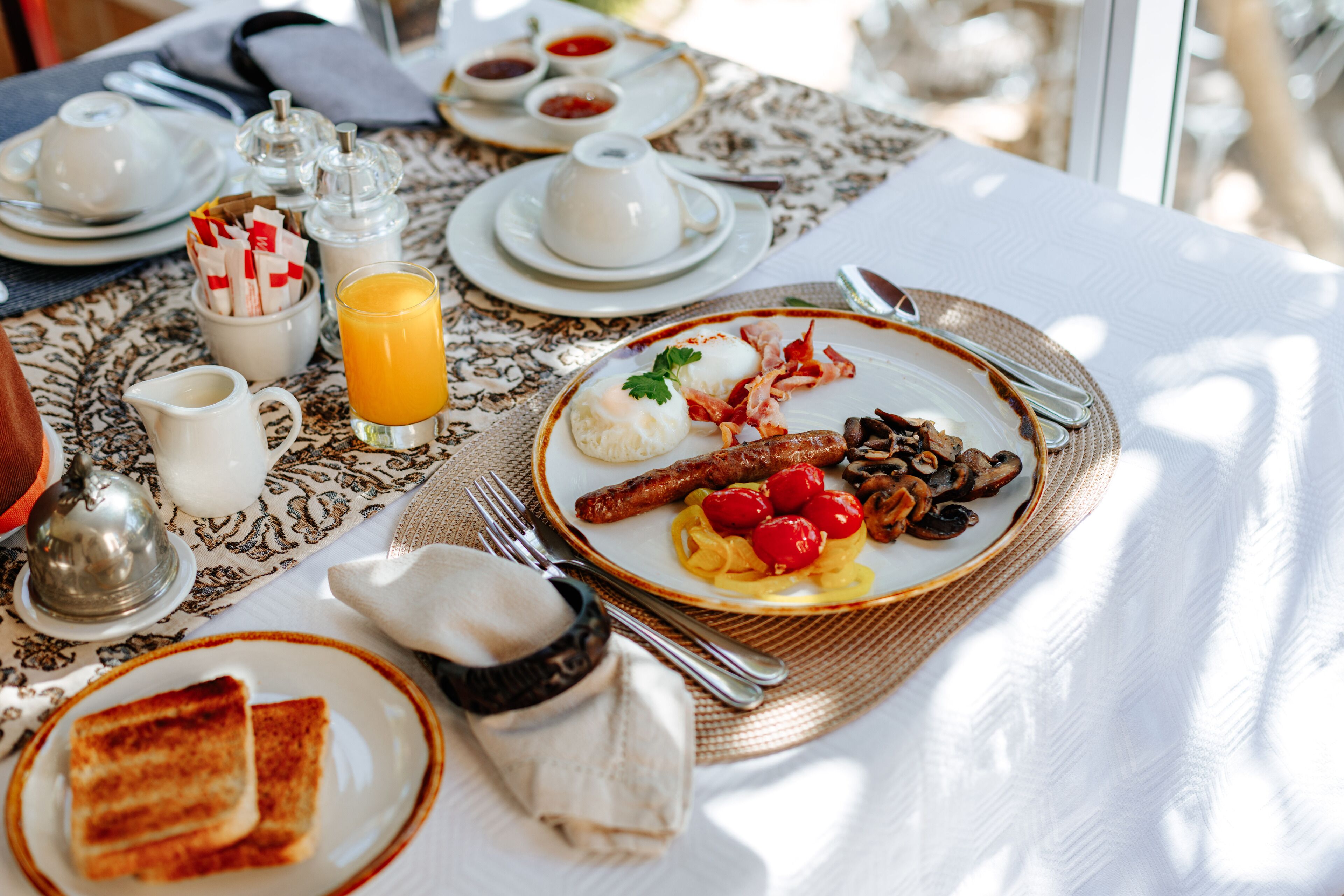 A breakfast table with plates of food, a jug of orange juice, and various condiments.