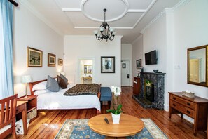 A well-lit bedroom with a bed, bedside table, lamp, and a round wooden table with a plant.