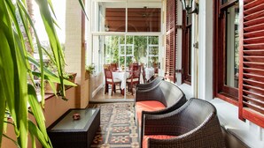 Un patio couvert, aménagé avec des meubles en osier, un sol carrelé et offrant une vue sur un espace de restauration extérieur.