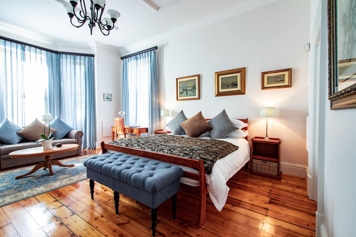 Ein Schlafzimmer mit einem hölzernen Bett, einer blauen Bank, einem Sofa und einem kleinen Tisch mit einer Pflanze.