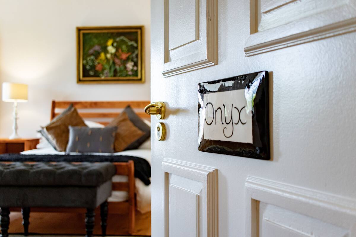 Ein Schlafzimmer mit einem Bett, Kissen, einem Nachttisch, einer Lampe und einer Tür mit dem Schild 'Onyx'.