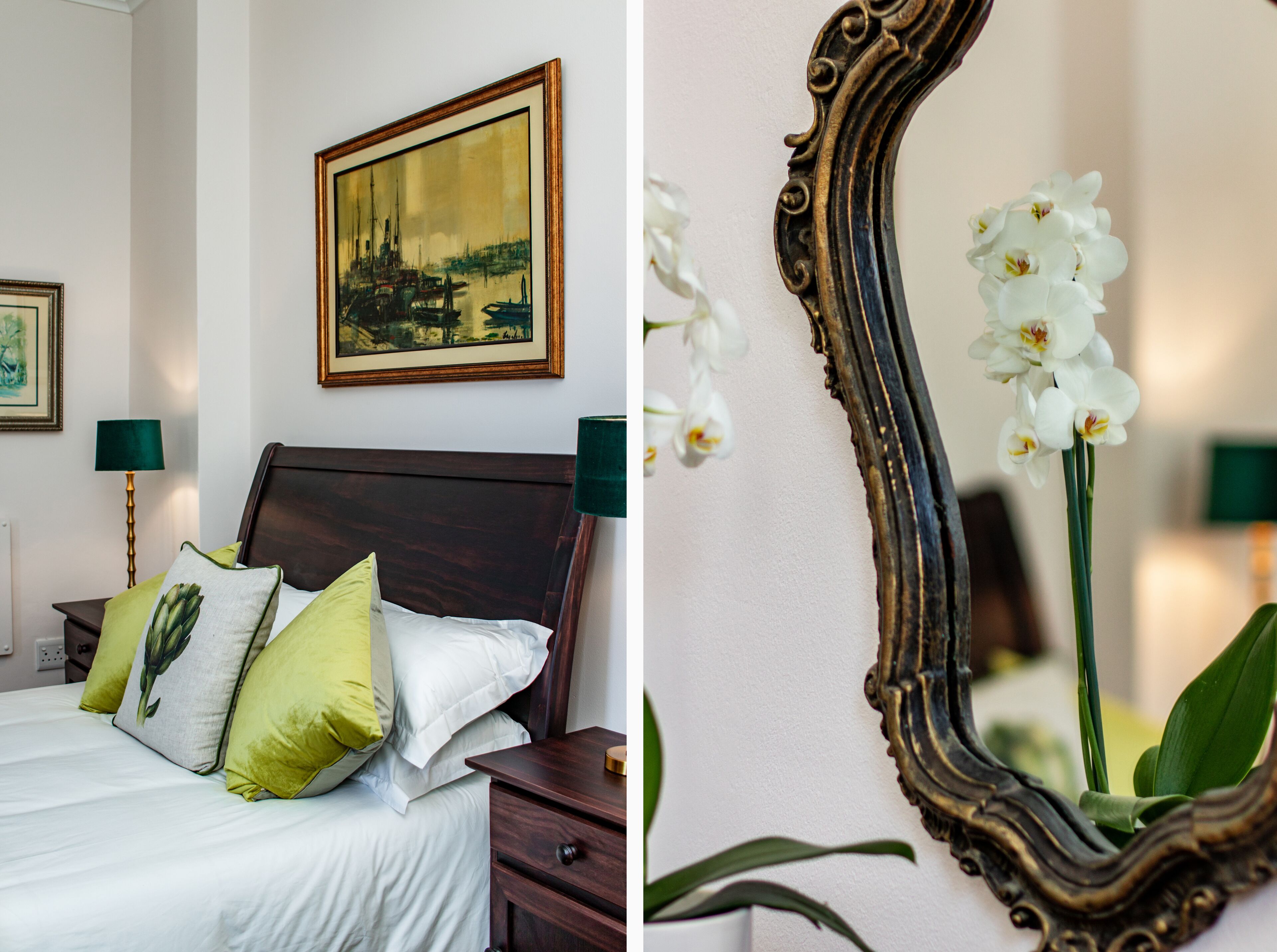 A neatly made bed with pillows, a framed painting above it, and a mirror with an orchid.