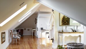 Une chambre spacieuse située dans les combles, avec un plancher en bois, une grande fenêtre, une coiffeuse avec un miroir et un peignoir suspendu.
