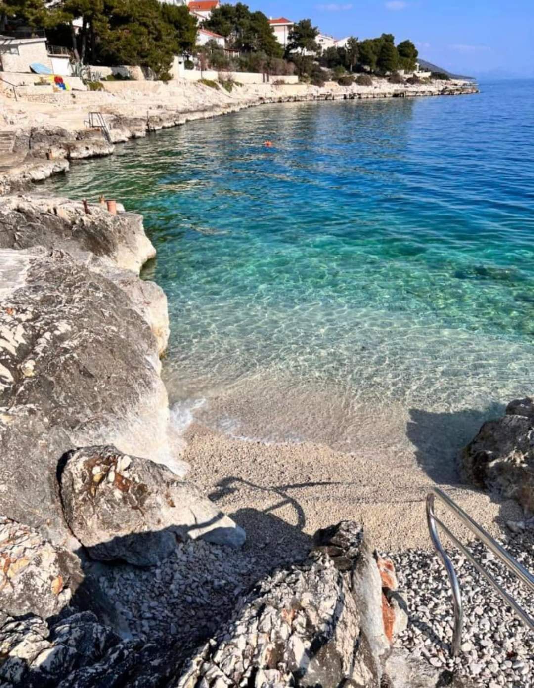 Un paysage côtier avec une eau bleue et limpide, une côte rocheuse et une promenade pavée.