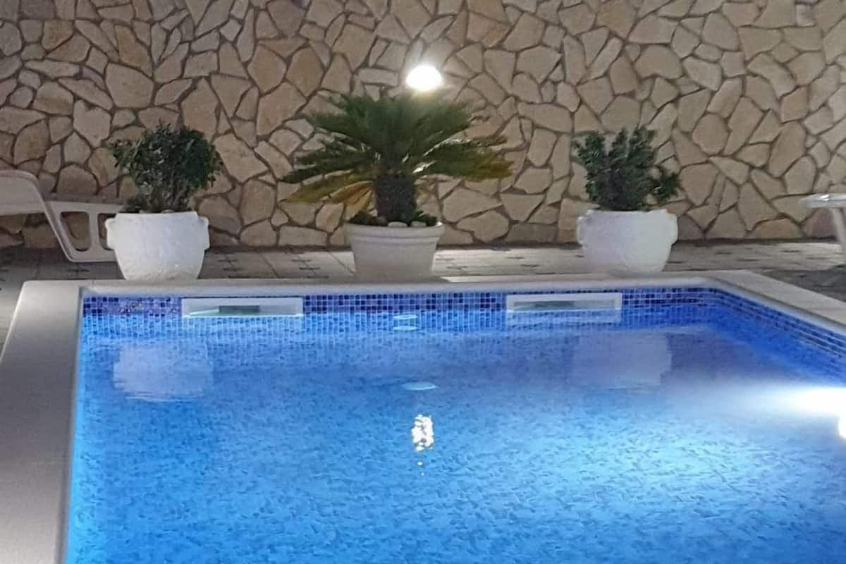 A swimming pool with a stone wall and potted plants.