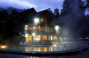 Uma pousada com piscina, espreguiçadeiras e montanhas ao fundo.