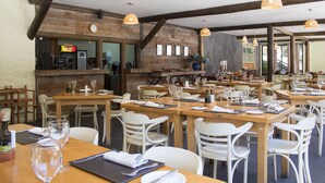 Un restaurante con mesas de madera y sillas blancas, una zona de bar y un reloj en la pared.