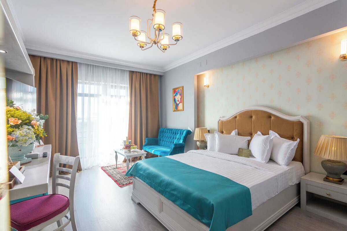 Habitación de hotel con una cama grande, un escritorio, una silla, una lámpara de escritorio, una mesita de noche y una ventana con cortinas.