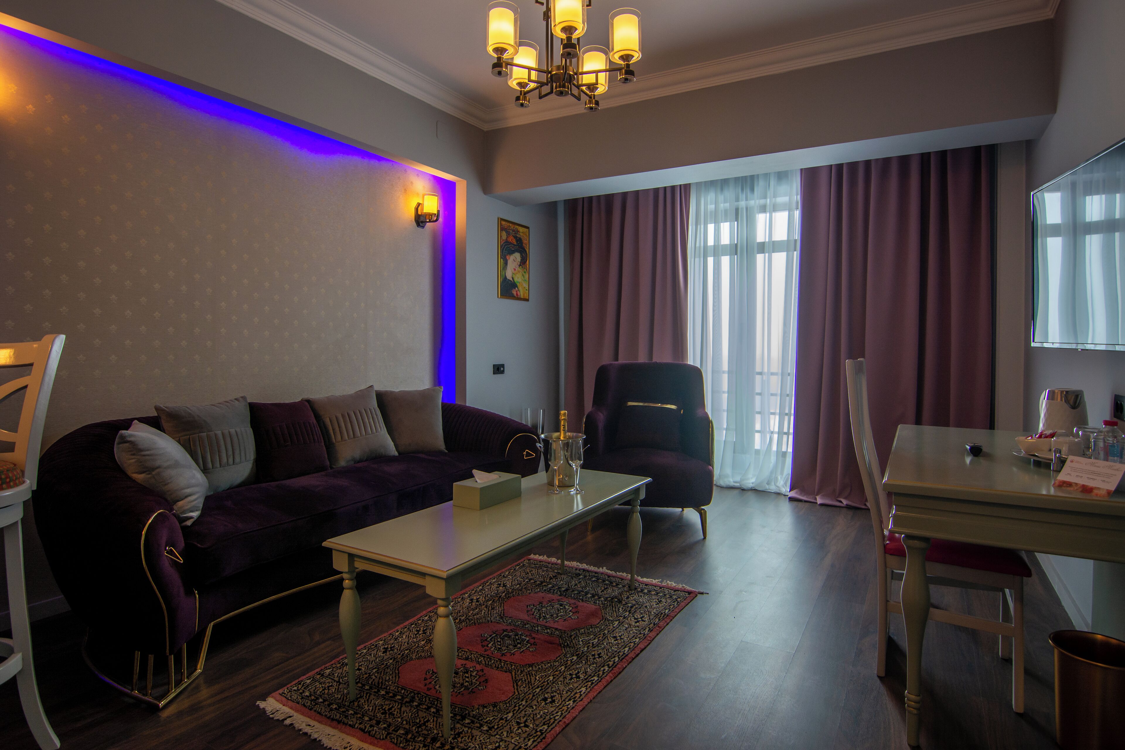 A living room with a dark purple sofa, a white coffee table, a dining table with chairs, and a chandelier.
