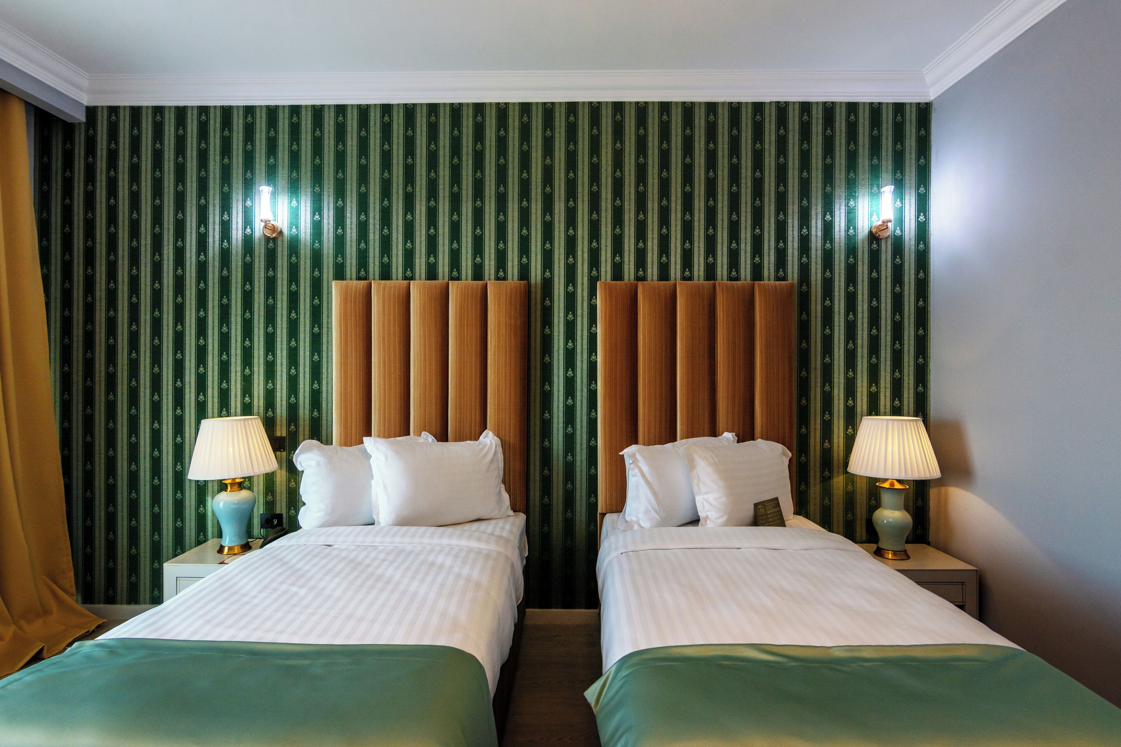 A hotel room with two beds, green striped wallpaper, and a wooden headboard.