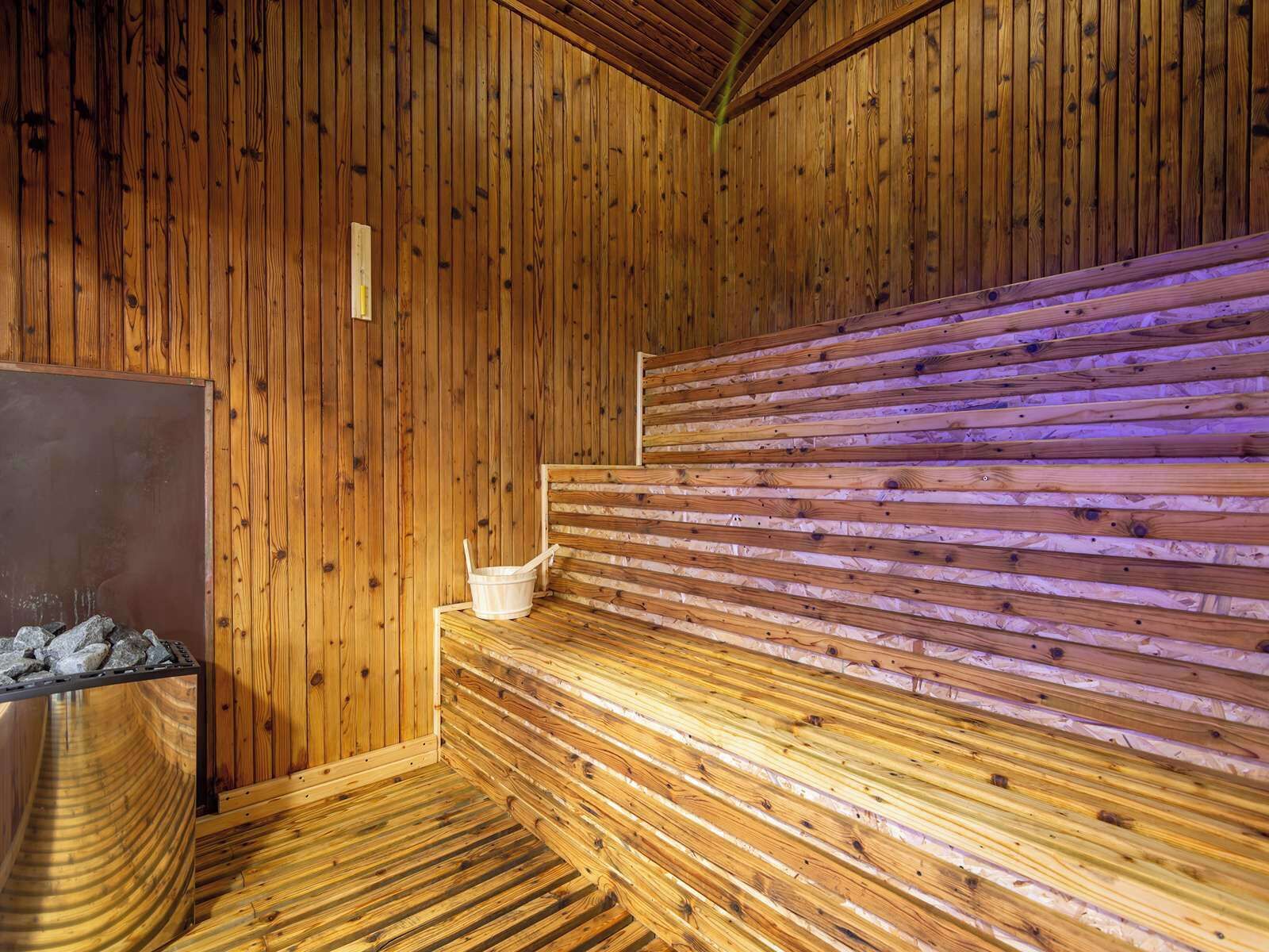 Una sauna con paredes y bancos de madera, una pileta de piedra y un recipiente de metal.