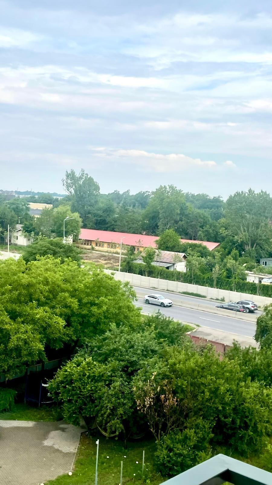 A view of a road with cars, surrounded by greenery and buildings with red roofs.
