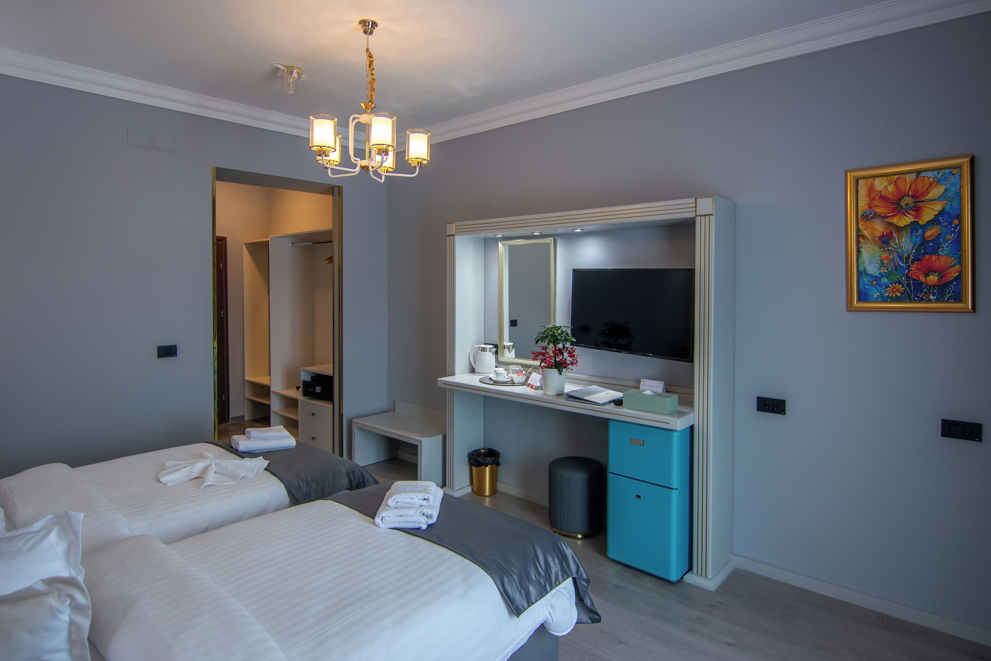 A hotel room with two beds, a desk with a mirror, a trash can, and a painting on the wall.