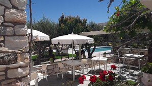 An outdoor patio with stone walls, white umbrellas, and potted plants. - Sunset Studios & Apartments - Adults Only (Paros)