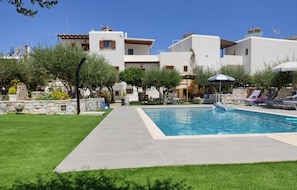 A swimming pool surrounded by a well-maintained lawn and trees, with buildings in the background.