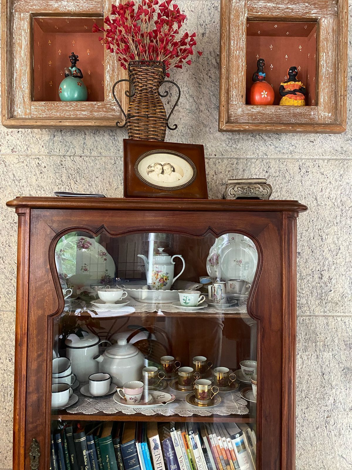 A wooden cabinet with glass doors displaying tea sets, books, and decorative items.