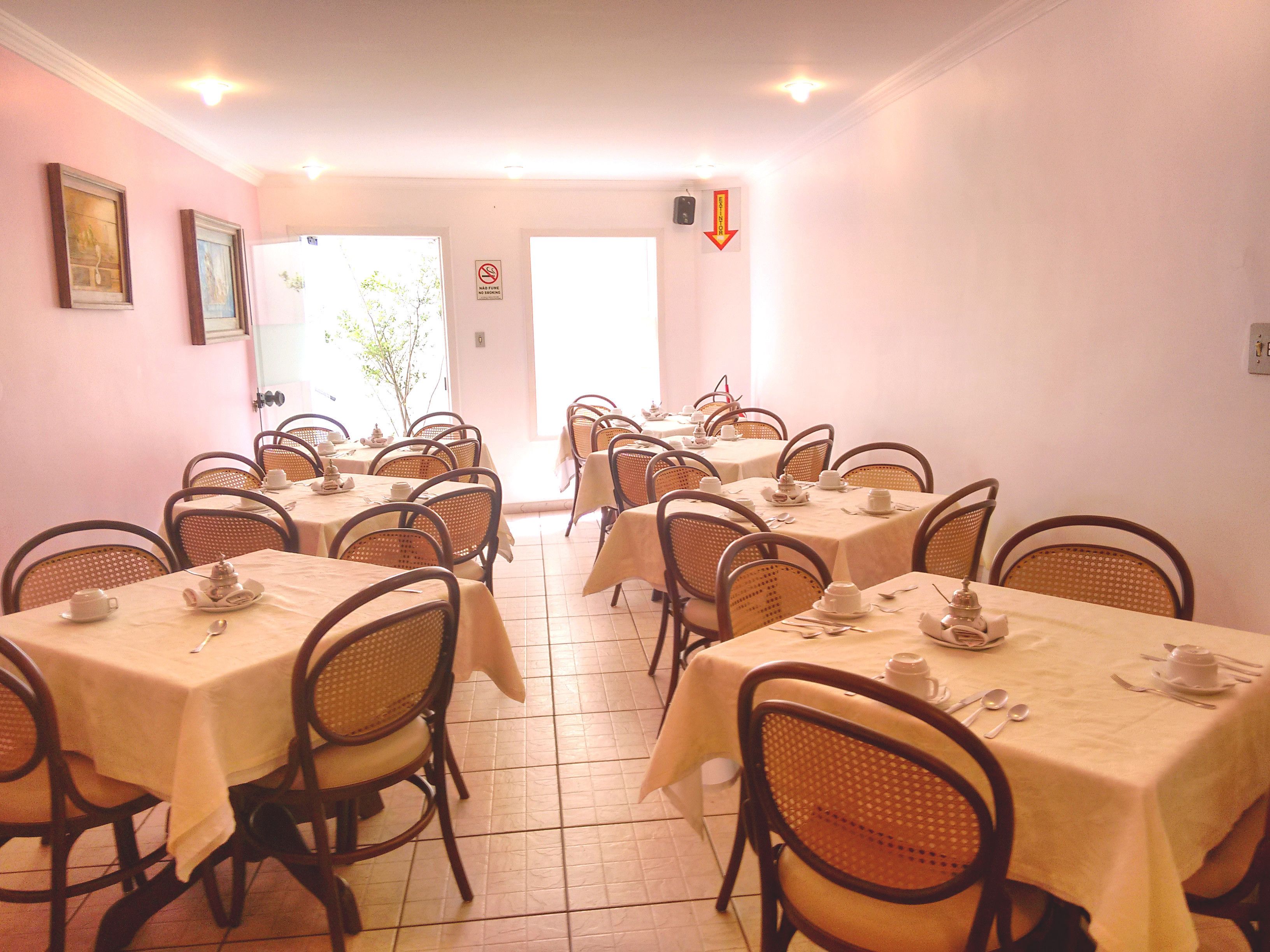 Un espace repas avec plusieurs tables préparées pour le service du thé, des chaises en osier et une vue sur l’extérieur.