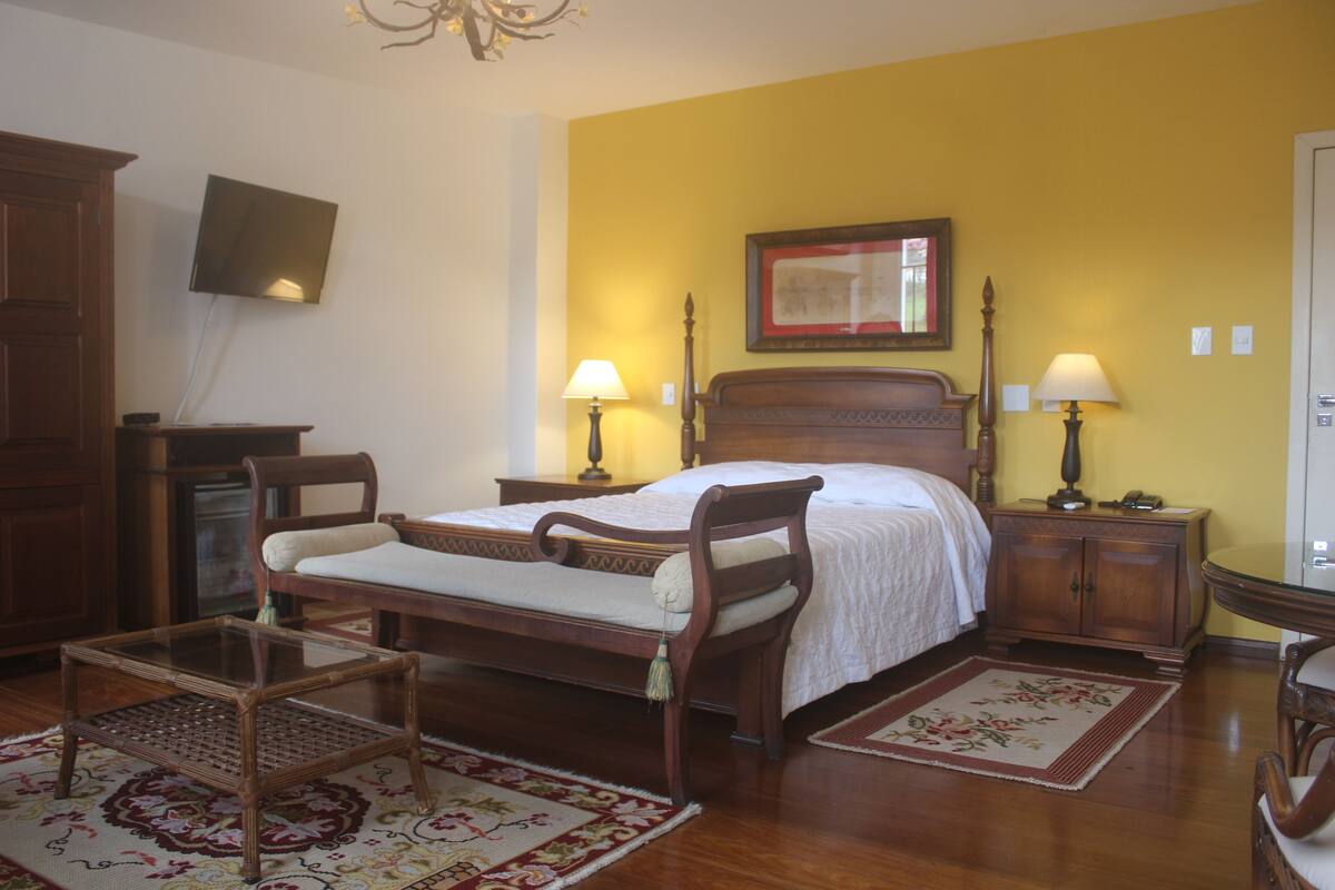 A bedroom with a wooden bed, two bedside tables with lamps, a TV on the wall, and a wooden wardrobe.