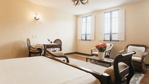 A hotel room with a large bed, two chairs, a small table, a chandelier, and two windows with shutters. - Pousada Minas Gerais (Ouro Preto)