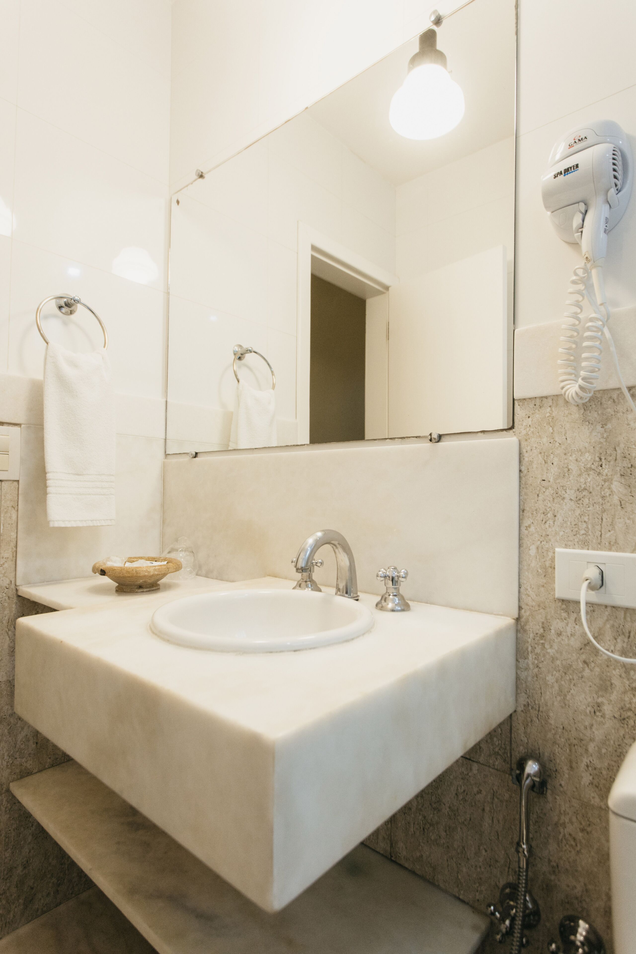 A bathroom with a white sink, a mirror, a towel rack, a hairdryer, and a shower.