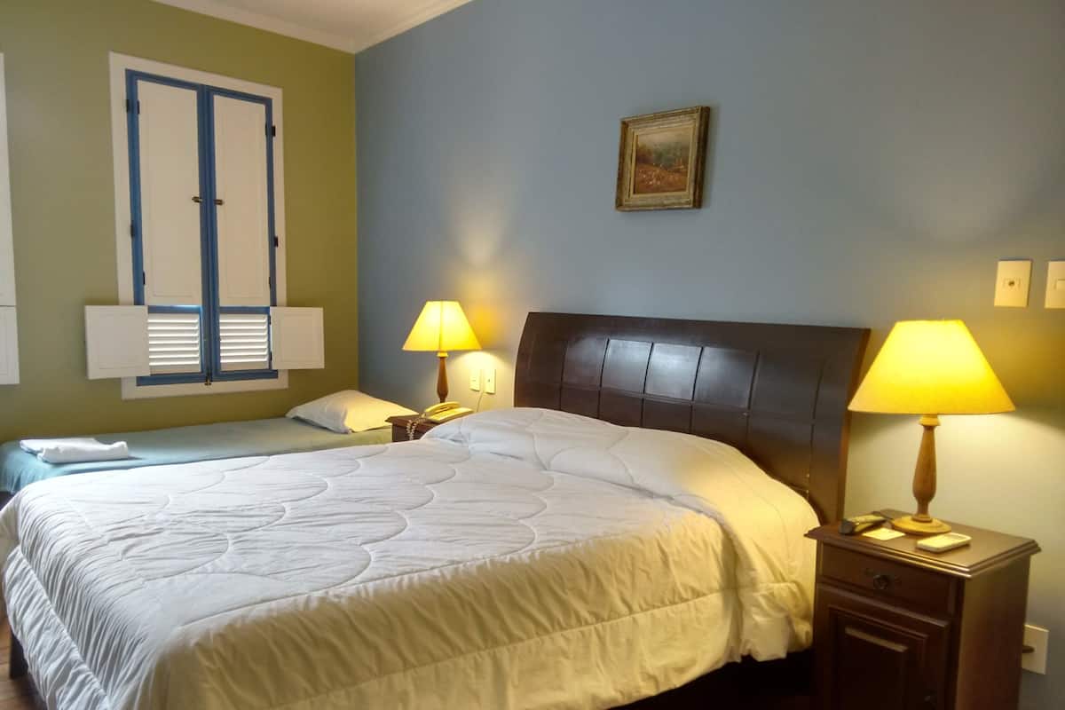A hotel room with a large bed, two bedside tables with lamps, a telephone, and a window with shutters.