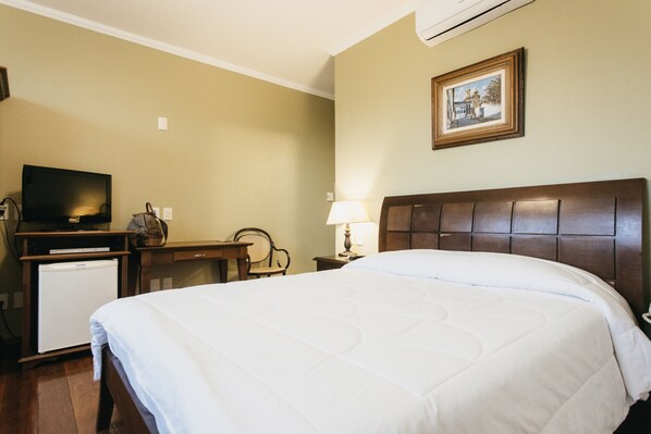A hotel room with a bed, a desk with a television, a lamp, and a small refrigerator. - Pousada Minas Gerais (Ouro Preto)
