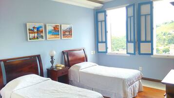 A room with two single beds, a nightstand with a lamp, a telephone, and three framed pictures on the wall.