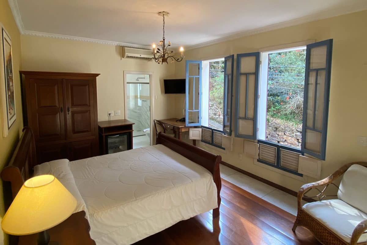 A bedroom with a large bed, wooden furniture, a desk, and a window with shutters.