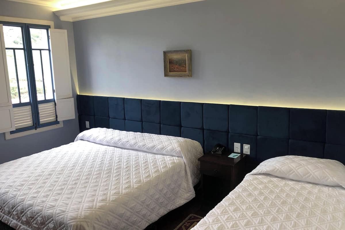 A hotel room with two beds, a nightstand, a framed picture on the wall, and a window with shutters.