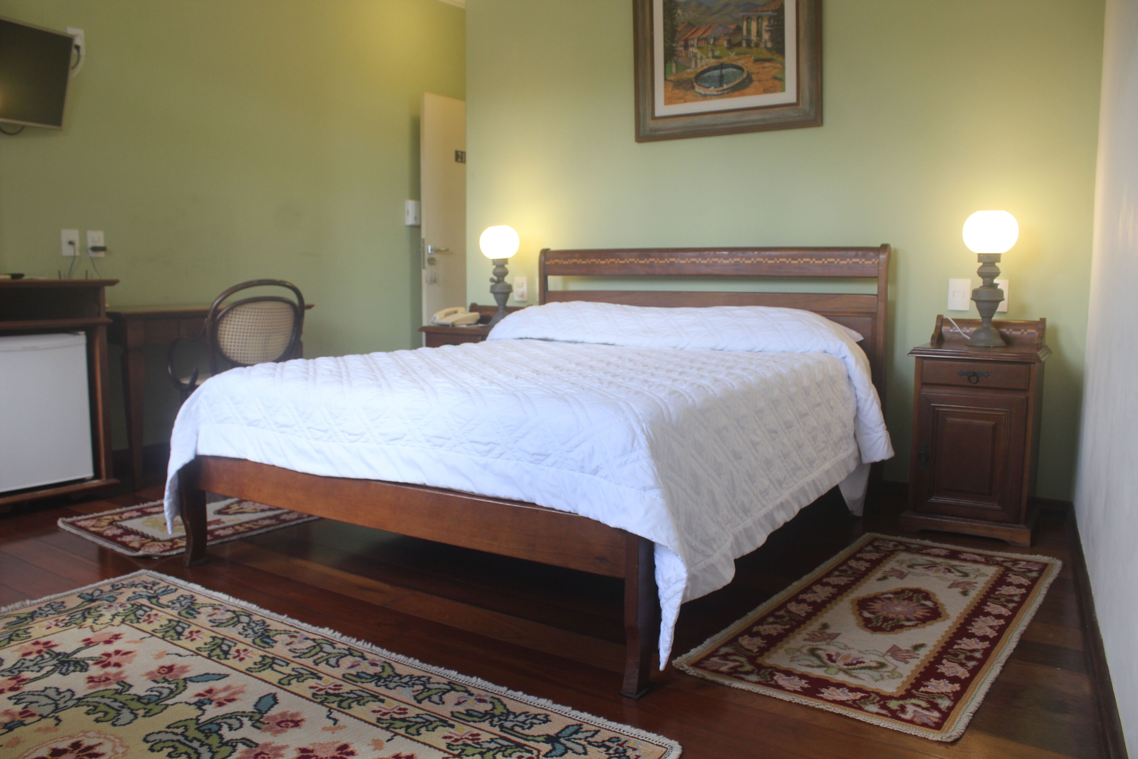 Una cama bien hecha con estructura de madera y ropa de cama blanca, flanqueada por dos mesitas de noche con lámparas.