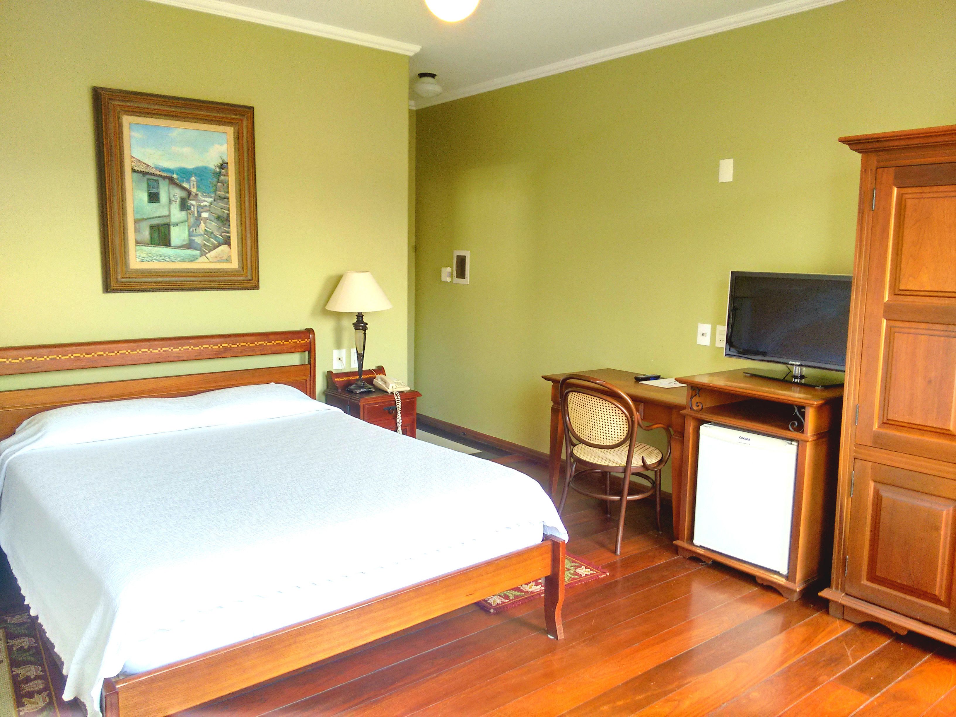 A hotel room with a bed, desk, chair, television, and a painting on the wall.