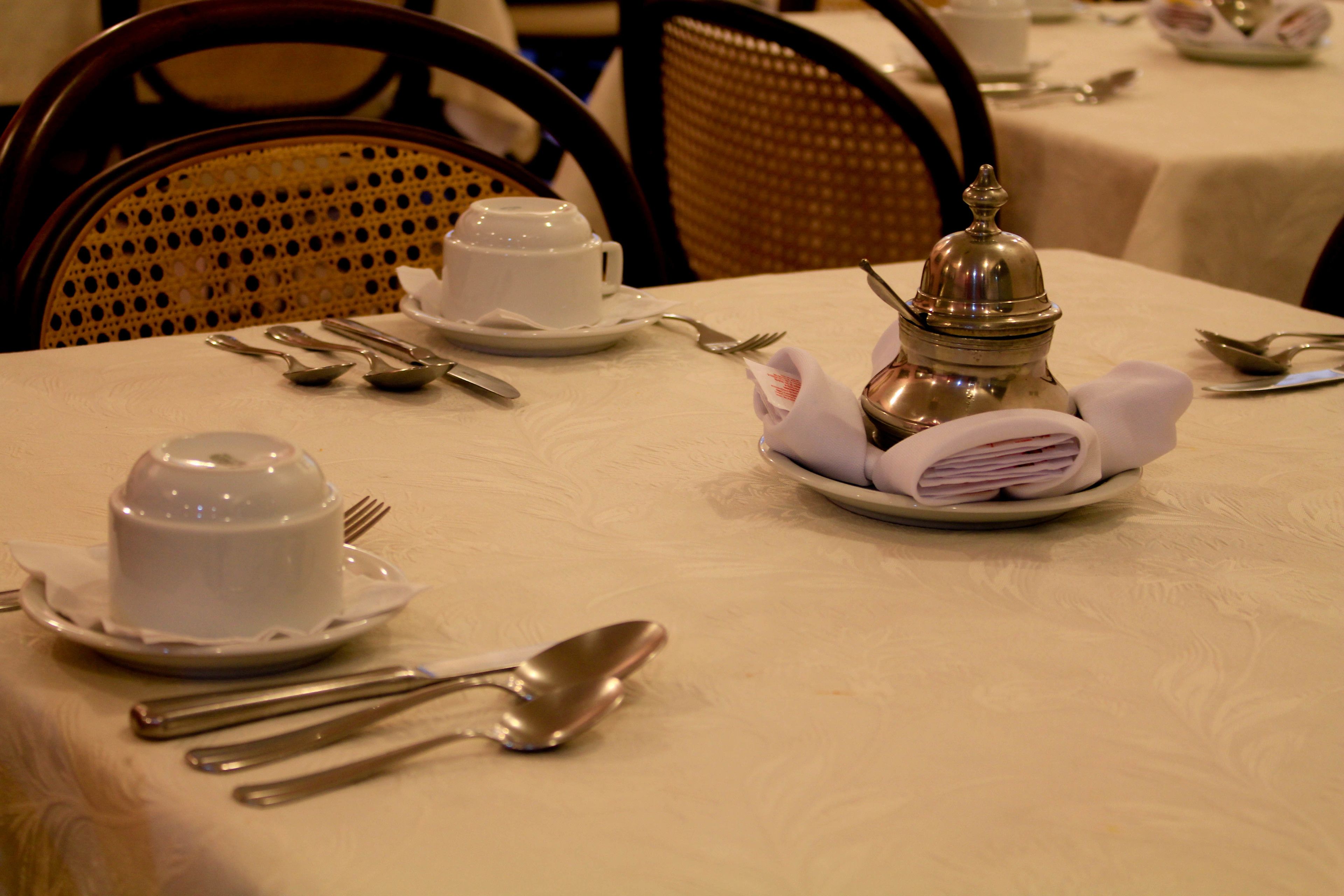 A dining table set with white tableware, including a teapot, cups, and cutlery.
