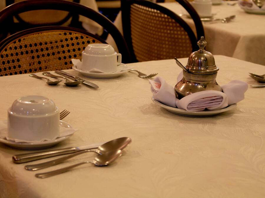 A dining table set with white tableware, including a teapot, cups, and cutlery.