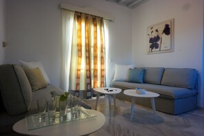 A modern living room with a grey sofa, a white coffee table, and a glass-topped side table. - Mykonos Chora Apartments (Mykonos)