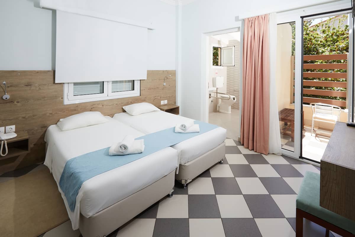 A hotel room with two beds, a checkered floor, a wooden headboard, a window, and a view of the outside.