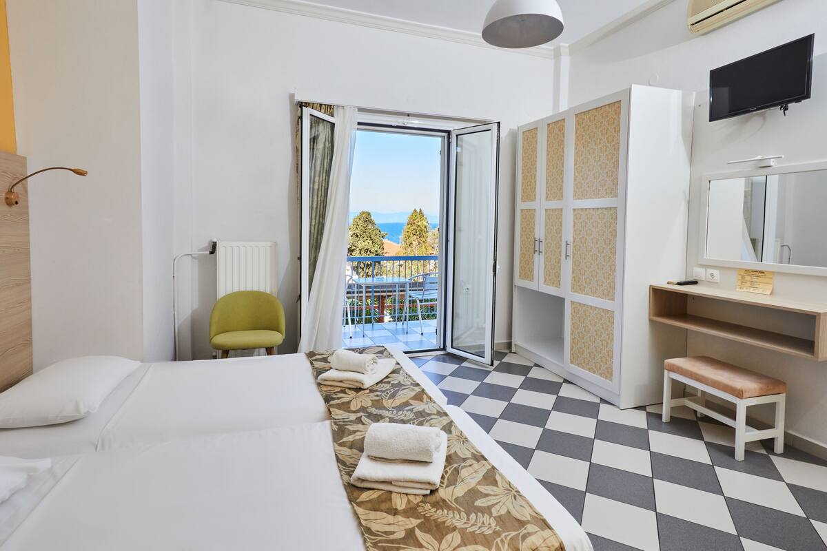 A hotel room with a bed, a bench, a chair, a TV, a desk, and a view of the outdoors.