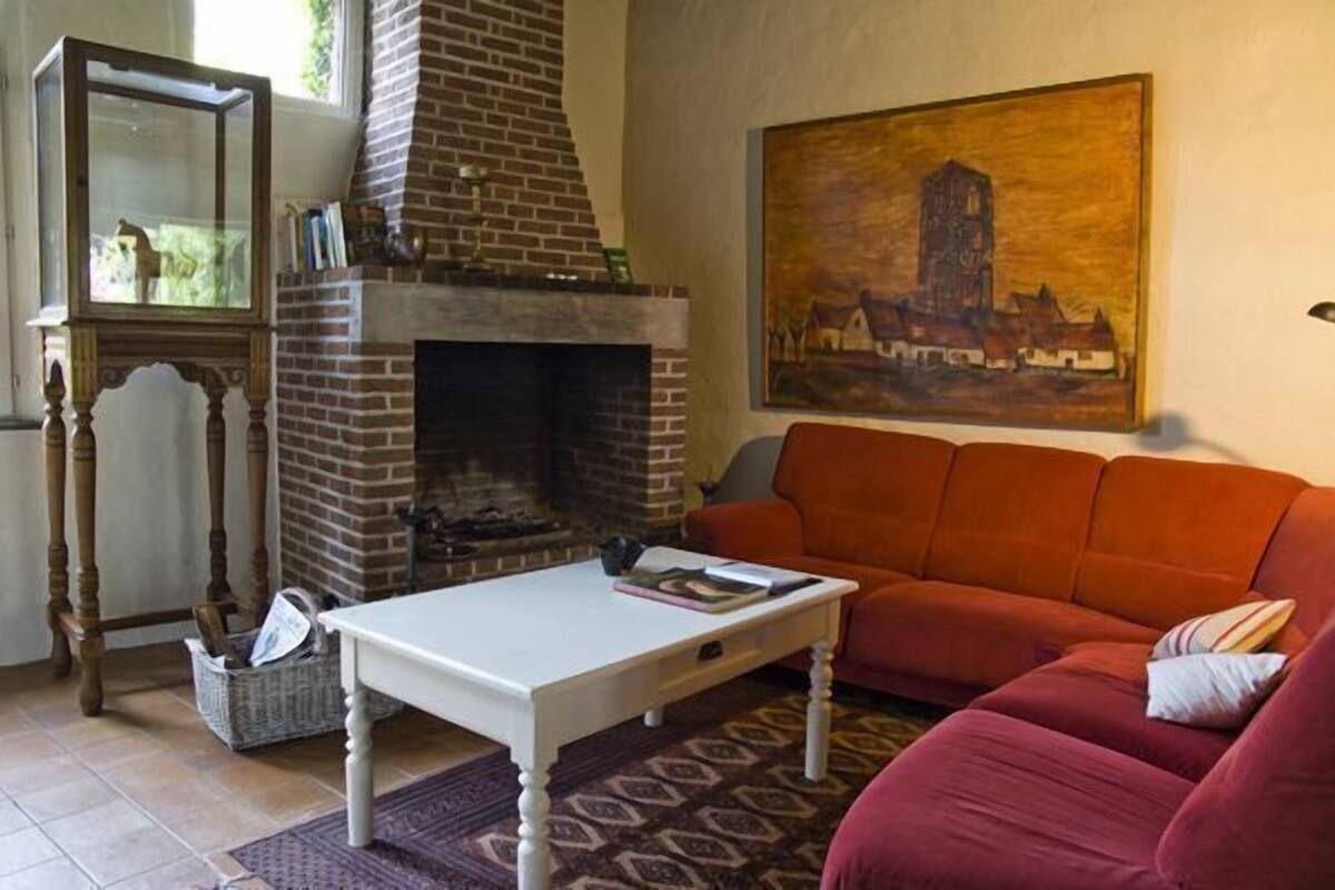Un salon avec une cheminée en briques, un canapé rouge et un tableau accroché au mur.