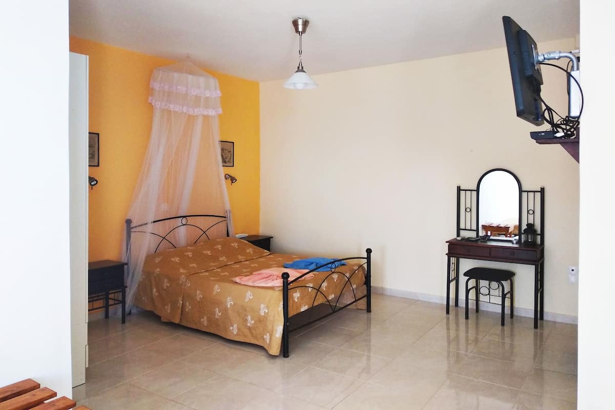 Ein Schlafzimmer mit Bett, Schreibtisch, Stuhl, Fernseher und Deckenventilator.