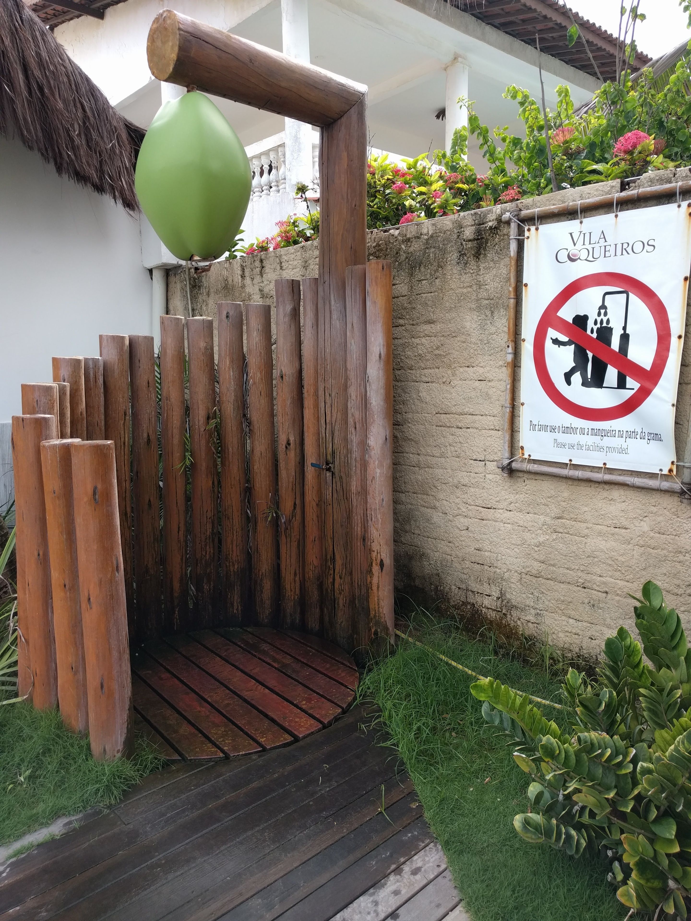 Ein hölzernes Tor mit einem grünen Ballon, einem Rauchverbotsschild und einer mit Pflanzen bepflanzten Mauer.