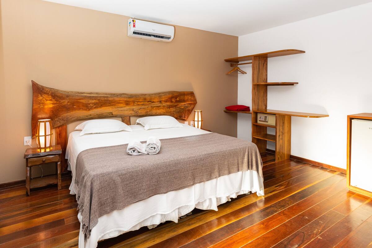 A neatly made bed with a wooden headboard, a bedside table with a lamp, and a wooden shelf unit against the wall.