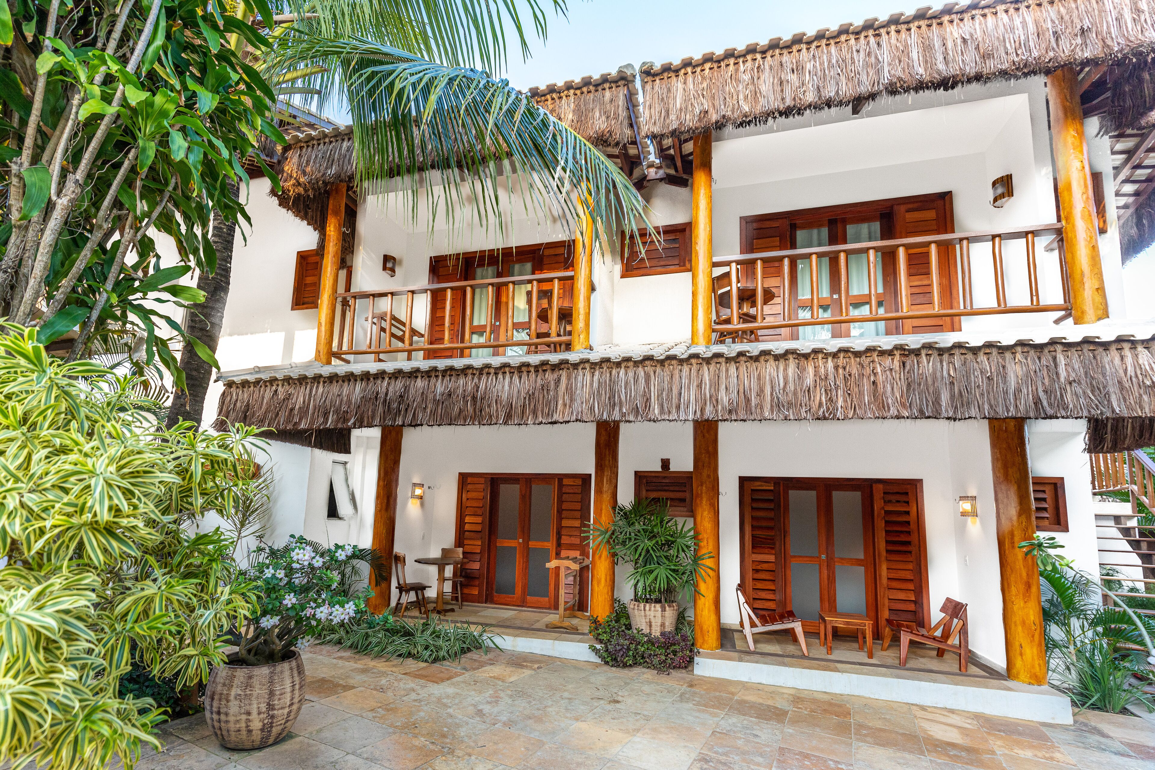 A two-story building with a thatched roof, wooden balconies, and a stone-paved courtyard.